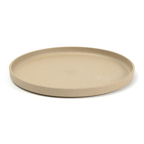 3/4 view of a round, tan plate on a white background. The color and texture is like pressed sand. Plate has straight sides with a lip protruding above the flat surface.